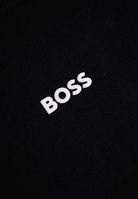 Lettres majuscules blanches formant le mot « BOSS » sur un fond en tissu noir texturé.