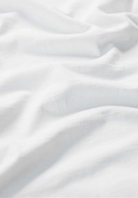 Fehér szövet, amely puha, sima felületű, finom redőkkel és hajtásokkal, ami könnyű anyagra és letisztult, minimalista dizájnra utal.