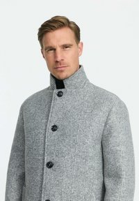 Hallide ruuduline villane mantel kõrge kraega, mustade nuppudega ja sileda tekstuuriga, millel on diagonaalsed ja vertikaalsed mustrid.