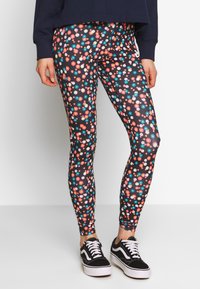 Blommönstrade leggings på en marinblå bakgrund med flerfärgade blommor. Materialet är elastiskt och kombineras med svarta sneakers.