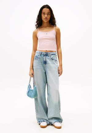 Helles rosa Tanktop mit dünnen Trägern, weit geschnittene hellblaue Jeans und eine kleine blaue gewebte Handtasche, kombiniert mit weißen Sneakers.