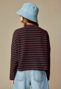 Marineblauwe gestreepte trui met rode lijnen, losse pasvorm en verlaagde schouders; gecombineerd met lichtblauwe denim shorts met hoge taille en een lichtblauwe bucket hat.