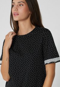 Černý krátký rukáv top s bílými puntíky; má krajkové detaily na rukávech a kulatý výstřih; vyrobeno z lehkého materiálu.