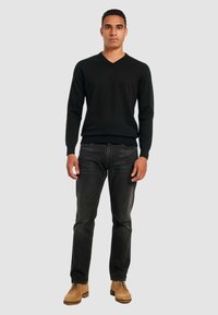 Black knitted V-neck sweater, fitted cuffs and hem, paired with dark jeans and tan lace-up shoes. Simple design with a smooth texture.