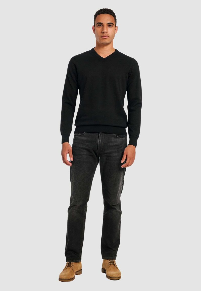 Black knitted V-neck sweater, fitted cuffs and hem, paired with dark jeans and tan lace-up shoes. Simple design with a smooth texture.