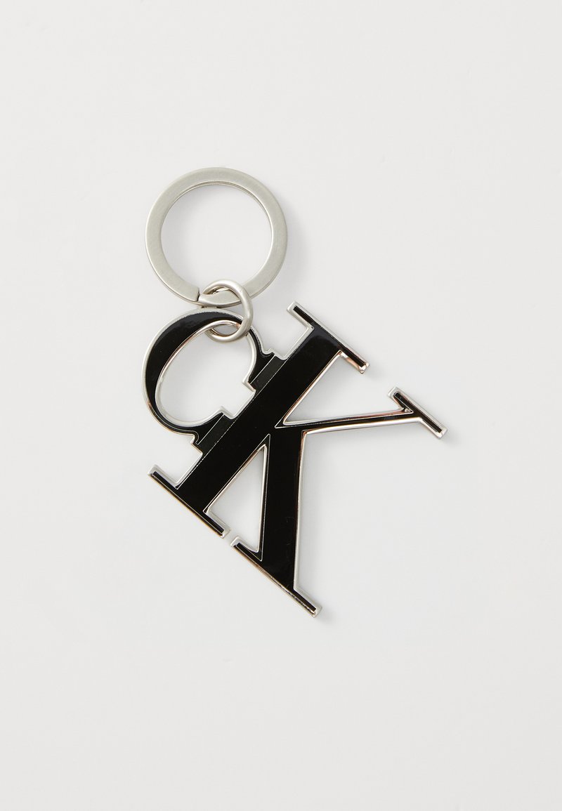Porte-clés en métal noir avec les lettres "CK" dans un design audacieux. Il comprend un anneau en argent pour l'attache. Texture lisse et finition brillante.