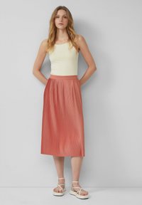 Plissé midi rok in koraaloranje, gemaakt van lichte stof, met een gladde tailleband; gecombineerd met een lichtgele mouwloze top.