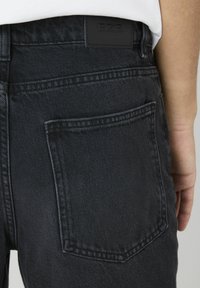 Pantalons en denim gris foncé avec une poche arrière et une étiquette BZB texturée noire au niveau de la taille. Le tissu présente un motif de tissage subtil.