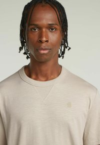 Felpa beige chiaro con scollatura rotonda a coste, tessuto testurizzato e sottile dettaglio del logo. La vestibilità è standard, con maniche di lunghezza media.