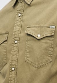 Khakifarbenes Hemd zum Knöpfen mit zwei vorderen Klappentaschen, Metall-Druckknöpfen und einem kleinen Jack & Jones-Label auf der Klappe der rechten Tasche.