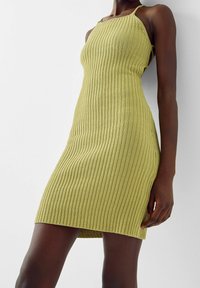 Abito in maglia a costine di un verde chiaro, con una silhouette attillata, spalline sottili e lunghezza a metà coscia, con dettaglio di spacco laterale.