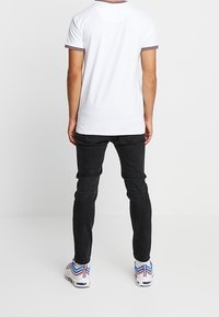 Valkoinen lyhythihainen paita, jossa on punainen ja sininen raidallinen kaulus, yhdistettynä mustiin slim fit -farkkuihin. Kengissä on monivärinen design.