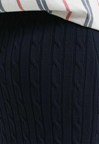 Gonna lavorata a maglia blu navy con un design a trecce testurizzato. Il tessuto ha un aspetto a coste, presentando motivi verticali e una texture liscia.