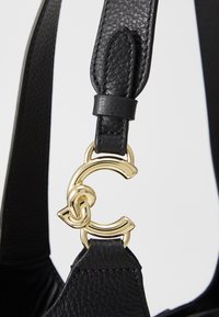 Black leather bag strap with a textured finish, featuring a gold C-shaped hardware accent and a secure leather loop attachment.