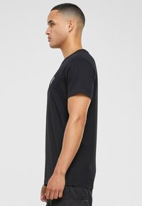 Black short-sleeve T-shirt in cotton, crew neck design, featuring a small graphic on the left chest and a straight cut. Simple and classic look.