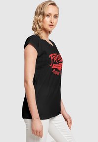 Schwarzes Baumwoll-T-Shirt mit kurzen Ärmeln, das ein rotes grafisches Design mit dem Text "FRIENDLY STRANGER" und "DON'T T" zeigt, im legeren Schnitt.
