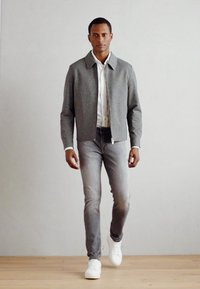 Chaqueta gris claro con cuello, camisa blanca debajo, combinada con jeans gris claro y zapatillas blancas; textura suave, diseño minimalista.