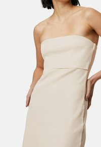 Robe beige sans bretelles avec texture côtelée, design ajusté et silhouette droite. Présente des coutures latérales et un style épuré et minimaliste.