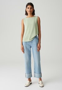 Top senza maniche verde chiaro con una leggera texture, abbinato a jeans a gamba larga blu chiaro con orli risvoltati, indossato con mocassini bianchi.