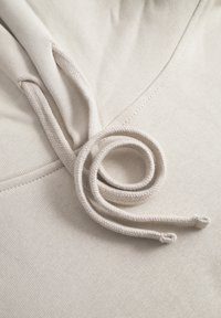 Beige cotton hoodie fabric with a textured surface; features a twisted drawstring coiled on top, highlighting its softness and seamless design.