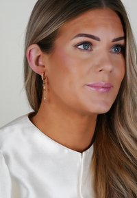 Guldtonade örhängen med hängande kedjor och blå ädelstenar. Bärs med en satinfärgad vit topp som framhäver accessoarens design.