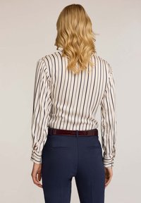 Langarmhemd in Creme mit navyblauen vertikalen Streifen, mit geknöpften Manschetten. Kombiniert mit navyblauen Hosen und einem glänzenden burgunderfarbenen Gürtel.