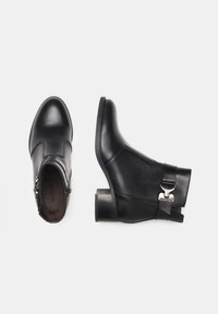 Bottines en cuir noir avec un bout rond, fermeture éclair sur le côté et quincaillerie décorative en métal. Présentent un petit talon épais et une finition lisse.