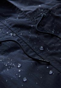 Gros plan sur un tissu imperméable bleu foncé avec des gouttes d'eau perlant à la surface et un cordon tressé noir avec une pointe en plastique.