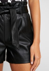 Svarta lädershorts med hög midja, med bälte och insydd elastisk detalj vid midjan. Slät textur och skräddarsydd passform.