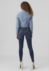 Svijetloplavi skraćeni traper jakna s dugim rukavima, detaljima na gumbima i glatkom teksturom. Uparena s tamnoplavim uskim trapericama i bež potpeticama.