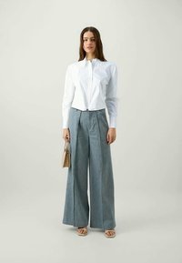 Άσπρο πουκάμισο με γιακά, ψηλόμεσες ανοιχτό γαλάζιες φαρδιές παντελόνες και μπεζ τσάντα. Λείο ύφασμα, ραμμένο με προσοχή, απλός σχεδιασμός.