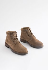 Hnedé semišové členkové topánky so šnurovaním, polstrovaným golierom, hrubou gumovou podrážkou a zosilneným prešívaním, vybavené šiestimi očkami a jemnou podšívkou.