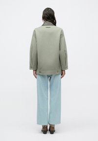 Prevelika svetlo zelena jakna z mehkimi tkaninami, ovratnikom in gumbi, kombinirana z širokimi svetlo modrimi kavbojkami.