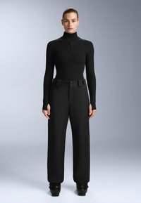 Svart ribbad polotröja med halvdragkedja och åtsittande ärmar, parat med vida svarta byxor med bälte i midjan och sidöppningar.