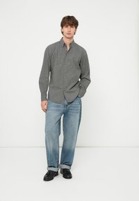 Szürke kockás gombos ing hosszú ujjakkal, laza kék farmernadrággal és fekete cipővel viselve. Egyszerű kialakítás klasszikus gallérral.