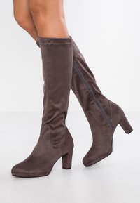 Botas altas de ante marrón con cremallera lateral, punta cuadrada y un tacón en bloque de 3 pulgadas. Presentan un discreto detalle de costura a lo largo de las costuras.