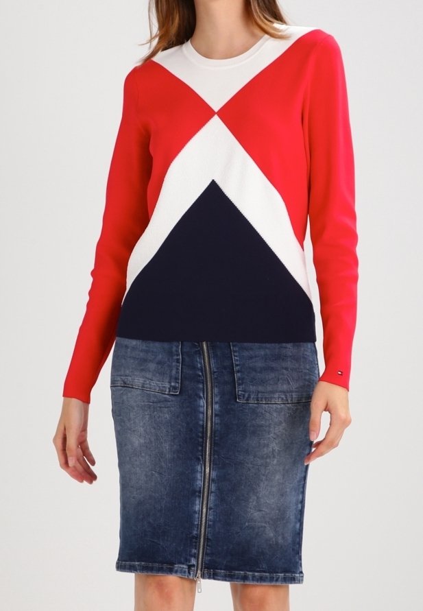 Femme portant un pull géométrique rouge, blanc et marine associé à une jupe crayon en denim délavé avec une fermeture éclair devant et des poches plaquées.