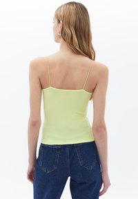 Canotta a costine gialla chiara con spalline sottili, abbinata a jeans a vita alta blu scuro con un design classico delle tasche.