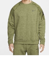 Homme portant un sweat-shirt Nike vert olive et un pantalon de survêtement assorti avec des logos Nike noirs, debout devant un fond blanc uni.