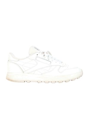 White low-top sneaker with laces and stitched detailing, flat sole with grip treads, displayed in side profile on a white background.
