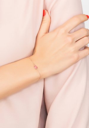 Delicate rose gold bracelet with a teardrop pink gemstone. Fine chain design enhances the elegant display on a soft, light fabric background.