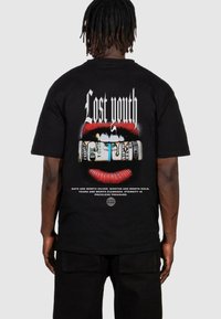 Sort bomulds t-shirt med et grafisk print på ryggen, der viser røde læber, der holder penge, med teksten "Tabt ungdom" ovenfor.
