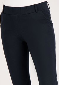 Navyblauwe taps toelopende broek van een zachte, rekbare stof met een gladde textuur, voorzien van zijzakken en een platte tailleband.