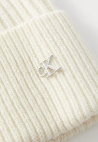 Beanie a righe crema in maglia con il logo CK argentato ricamato sul davanti. Tessuto morbido e tessuto elastico per una vestibilità comoda.