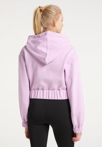 Lavendelcroppad hoodie med dragsko, elastisk nederkant och samlade mudd, tillverkad av mjukt material, tillsammans med svarta tights.