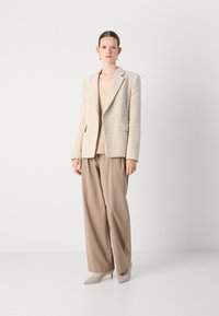 Beige tweed-blazer med notch-lapel, parret med en lys beige top, løse brune bukser og spidse beige hæle. Glat tekstur, skræddersyet pasform.