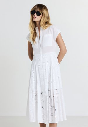 Weißes Baumwollkleid mit kurzen Ärmeln, Knopfleiste vorne und Stickereidetails. Verfügt über zwei Brusttaschen und einen ausgestellt geschnittenen Rock.