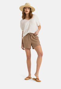 Blusa bianca, morbida e ampia con abbottonatura e maniche corte. Pantaloni corti marroni con cordoncino realizzati in un tessuto morbido e texturizzato. Sandali beige.