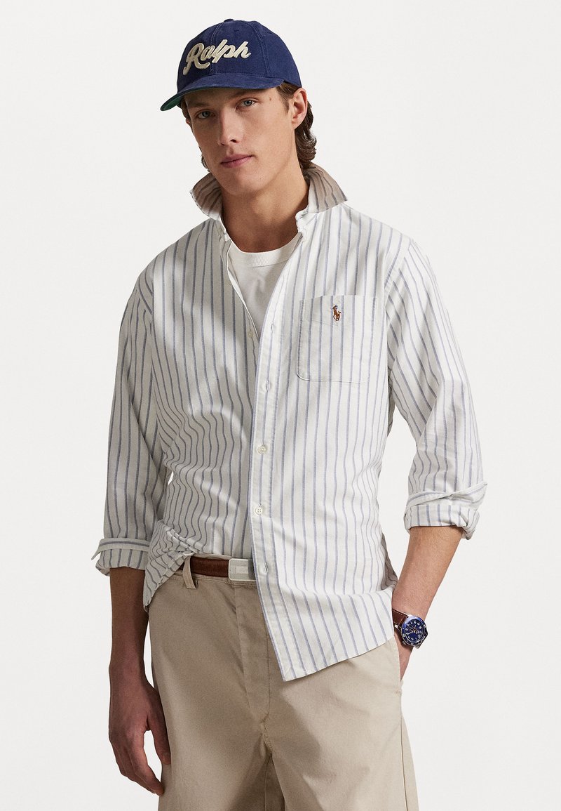 White button-up shirt with blue vertical stripes, rolled sleeves, and a pocket. Paired with a navy cap featuring "Ralph" in white lettering.