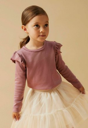 Camicia a maniche lunghe rosa chiaro con dettagli arricciati sulle spalle, abbinata a una gonna in tulle avorio a strati. Tessuto morbido, design casual.